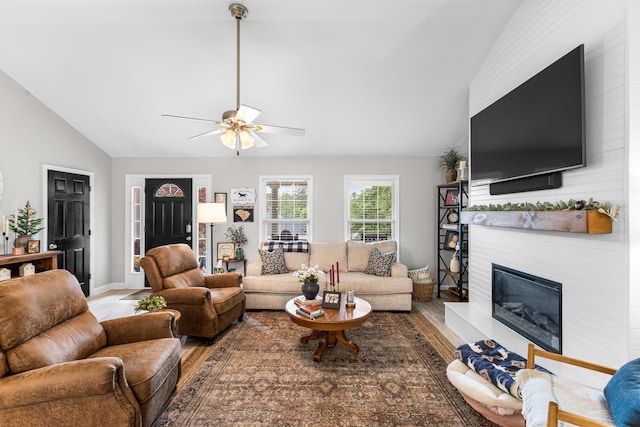 living area with wood finished floors, a large fireplace, a ceiling fan, and high vaulted ceiling