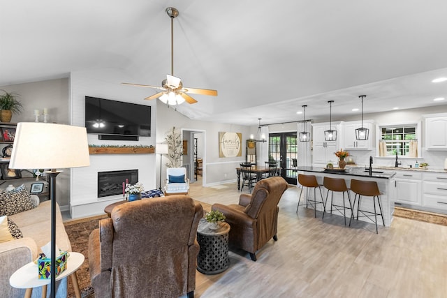 living area with vaulted ceiling, a large fireplace, a ceiling fan, light wood-style floors, and plenty of natural light