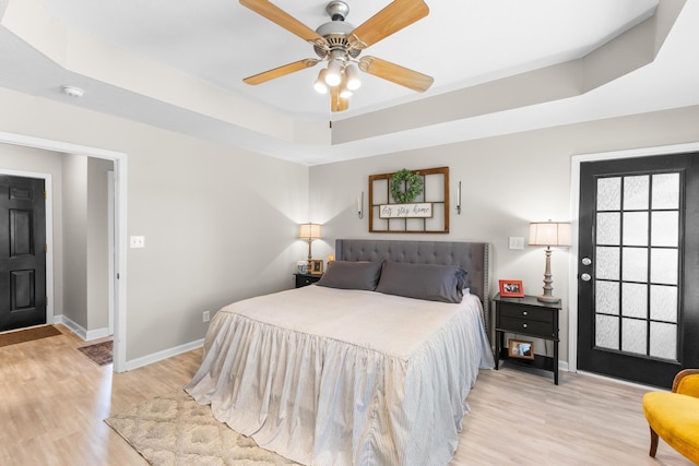 bedroom featuring baseboards, light wood-style flooring, a raised ceiling, and ceiling fan