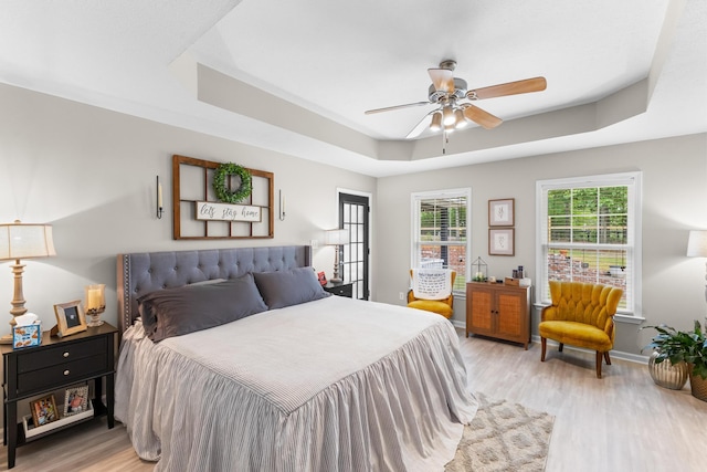 bedroom with light wood-type flooring, a raised ceiling, baseboards, and ceiling fan