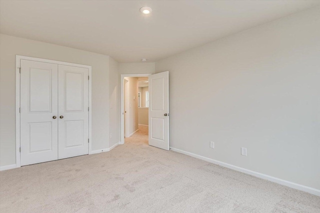 unfurnished bedroom with light carpet, a closet, and baseboards