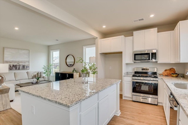 kitchen featuring light stone countertops, stainless steel appliances, white cabinetry, open floor plan, and a center island