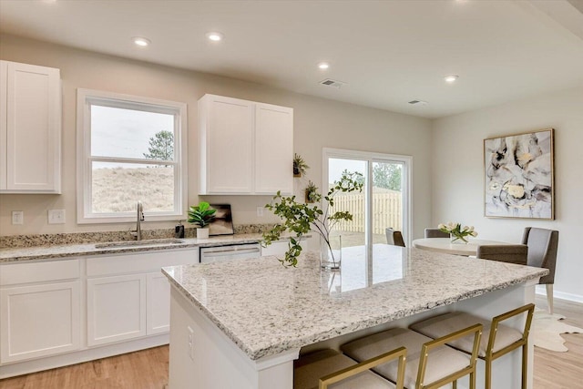 kitchen with light stone counters, a breakfast bar, a sink, a kitchen island, and white cabinets