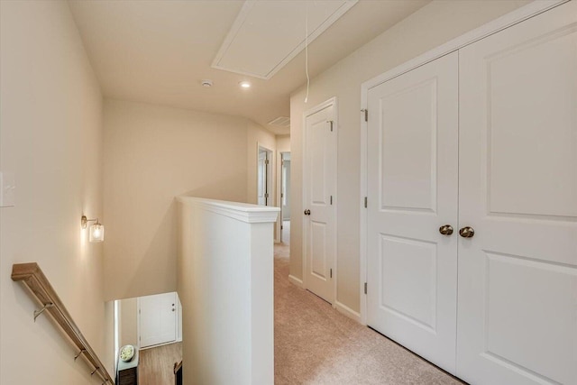 hall featuring attic access, baseboards, light carpet, and an upstairs landing