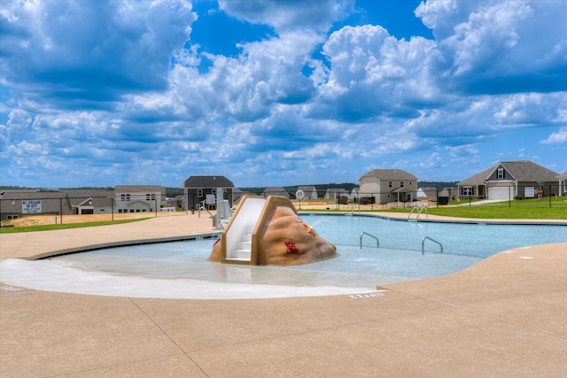 community pool with a water slide, fence, and a residential view