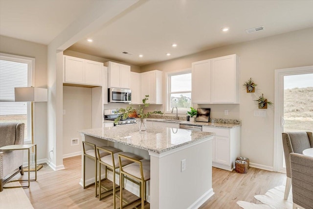 kitchen with stainless steel appliances, a sink, a kitchen island, white cabinetry, and light stone countertops