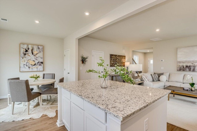 kitchen featuring light stone counters, a kitchen island, white cabinetry, open floor plan, and light wood-type flooring