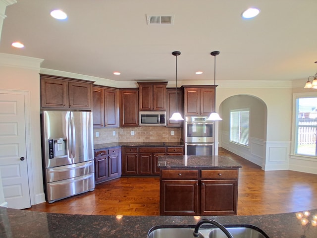 kitchen with appliances with stainless steel finishes, wainscoting, dark wood finished floors, and visible vents