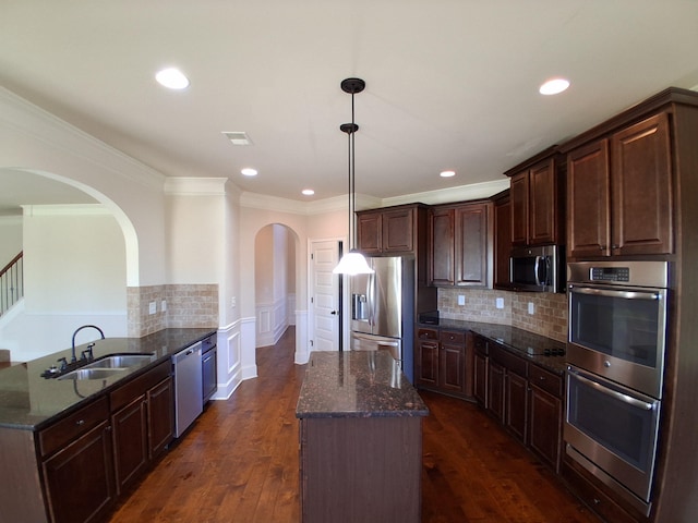 kitchen with dark stone counters, appliances with stainless steel finishes, dark wood-type flooring, a center island, and a sink