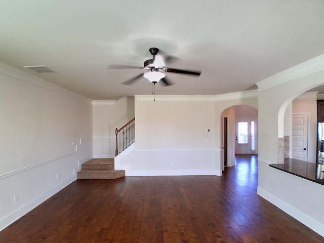 empty room featuring dark wood-style floors, arched walkways, crown molding, baseboards, and stairs