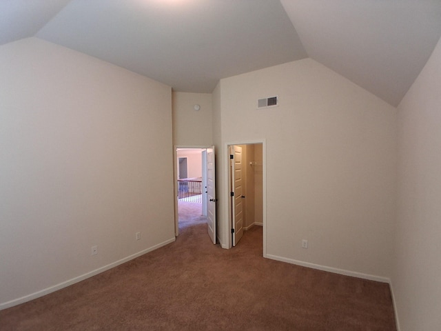 unfurnished bedroom featuring carpet, a walk in closet, visible vents, vaulted ceiling, and baseboards