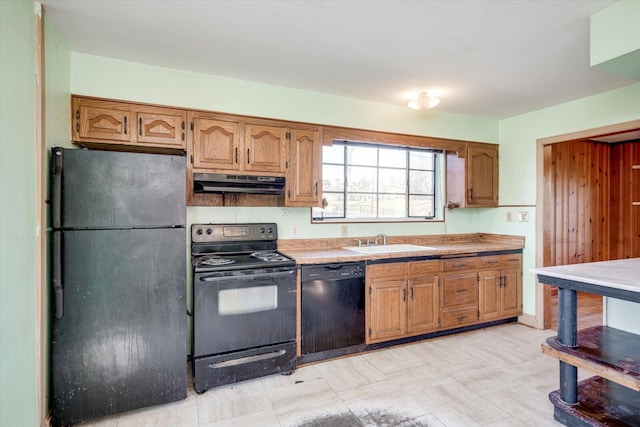 kitchen featuring brown cabinetry, a sink, black appliances, light countertops, and under cabinet range hood