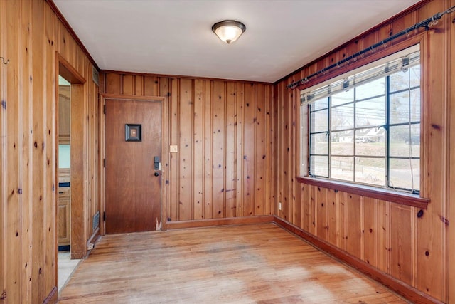 unfurnished room featuring wooden walls, baseboards, and light wood-type flooring