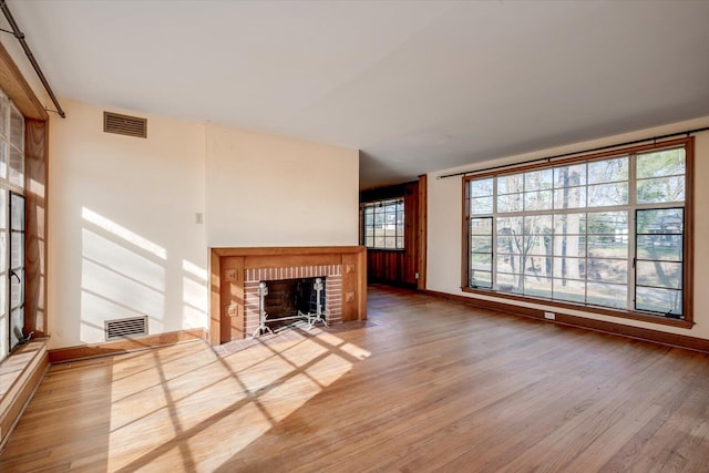 unfurnished living room featuring a brick fireplace, wood finished floors, visible vents, and baseboards