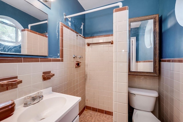 full bathroom with a wainscoted wall, tiled shower, a sink, tile walls, and toilet