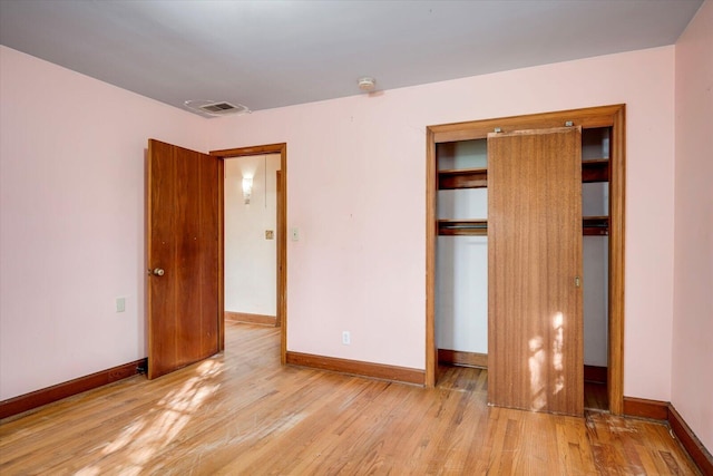 unfurnished bedroom featuring wood finished floors, visible vents, a closet, and baseboards