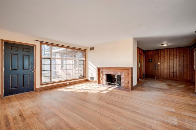 unfurnished living room featuring wood finished floors, visible vents, baseboards, a fireplace, and wood walls