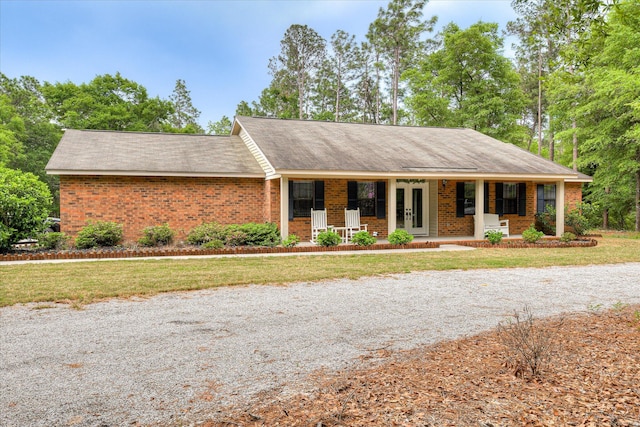 single story home featuring a front lawn, brick siding, roof with shingles, and covered porch