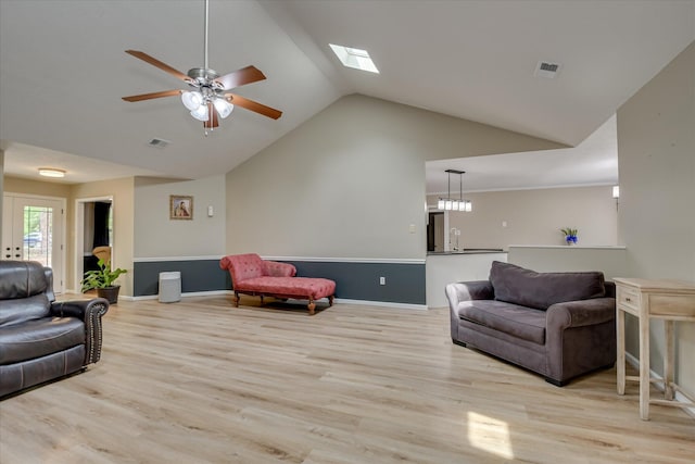 living room with wood finished floors, visible vents, baseboards, vaulted ceiling with skylight, and ceiling fan