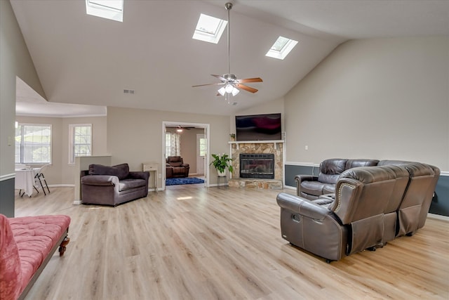 living area featuring visible vents, a ceiling fan, light wood-style floors, a skylight, and a fireplace