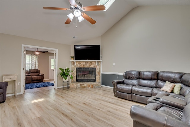 living area featuring lofted ceiling, a stone fireplace, ceiling fan, and wood finished floors