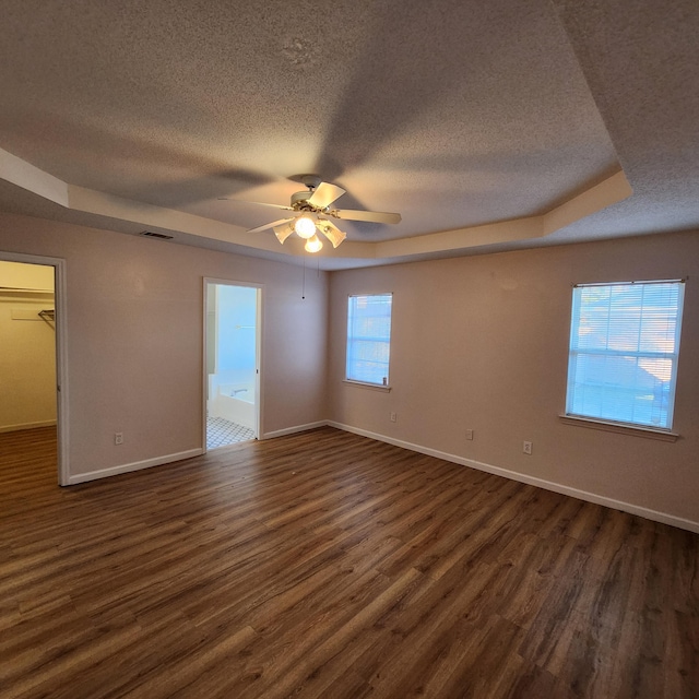 spare room with a textured ceiling, dark hardwood / wood-style flooring, a tray ceiling, and ceiling fan