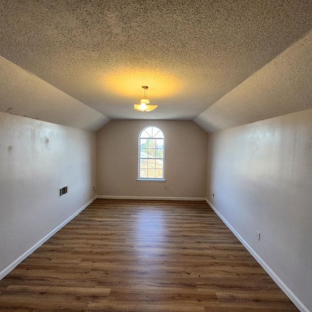 bonus room with a textured ceiling, vaulted ceiling, and dark wood-type flooring