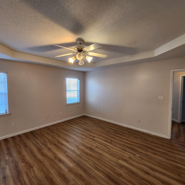 spare room with ceiling fan, dark hardwood / wood-style floors, a raised ceiling, and a textured ceiling