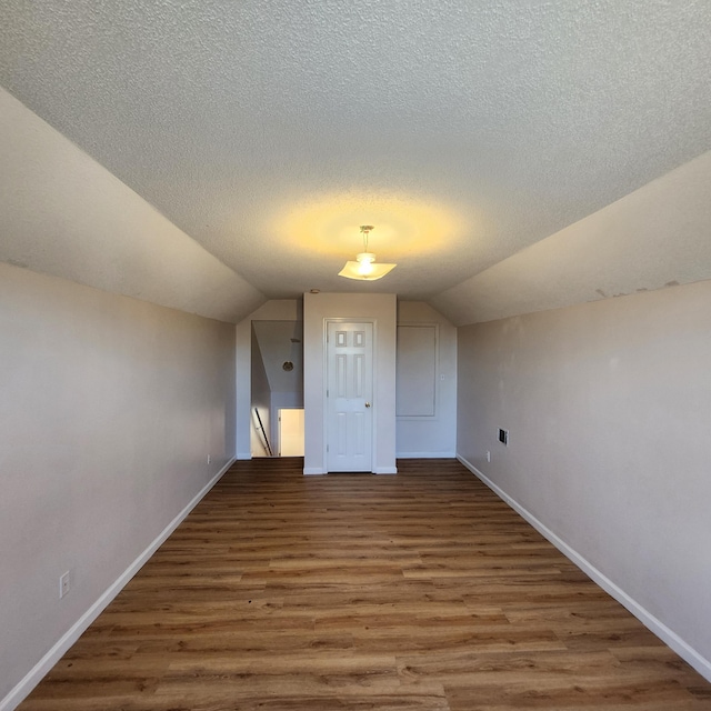 additional living space featuring dark hardwood / wood-style floors, lofted ceiling, and a textured ceiling