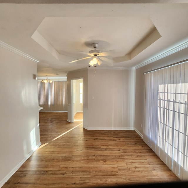 spare room with a tray ceiling, crown molding, light hardwood / wood-style flooring, and ceiling fan with notable chandelier