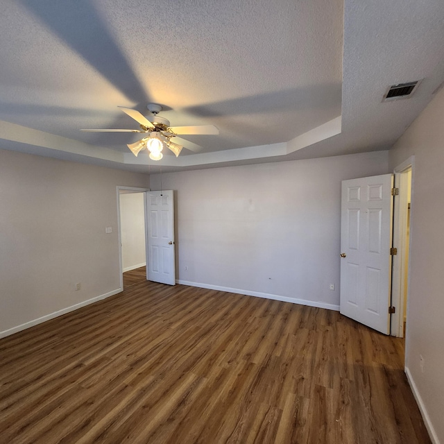 empty room with a textured ceiling, ceiling fan, a raised ceiling, and dark wood-type flooring