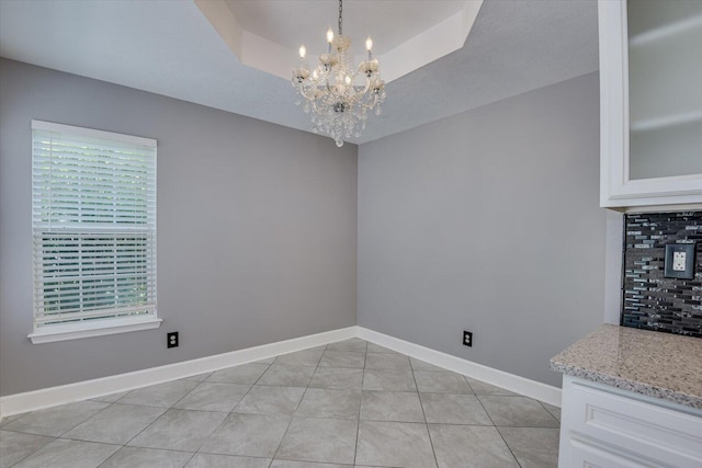 unfurnished dining area with light tile patterned floors, a tray ceiling, and a notable chandelier