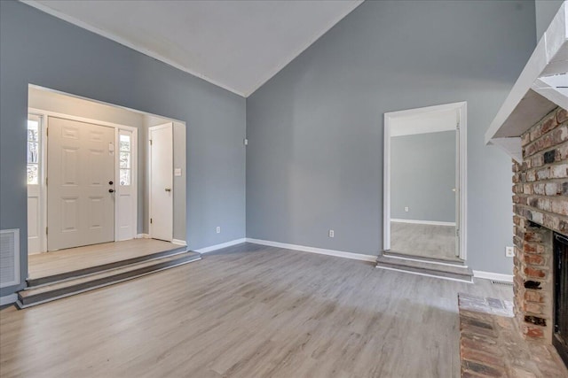 entryway with a fireplace, light hardwood / wood-style floors, and high vaulted ceiling