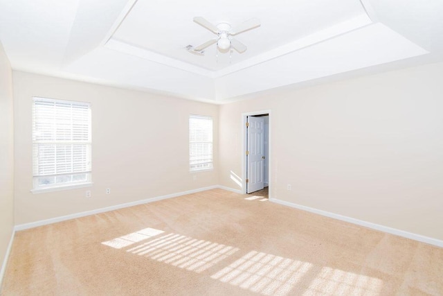 unfurnished room with ceiling fan, light carpet, and a tray ceiling