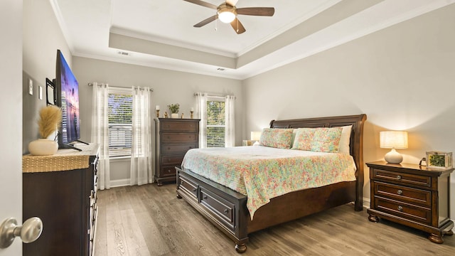 bedroom with hardwood / wood-style floors, a tray ceiling, ceiling fan, and crown molding