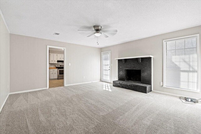 unfurnished living room with ceiling fan, a textured ceiling, light carpet, visible vents, and a brick fireplace