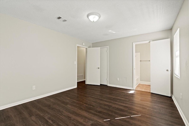 unfurnished bedroom with a textured ceiling, dark wood-type flooring, visible vents, and baseboards