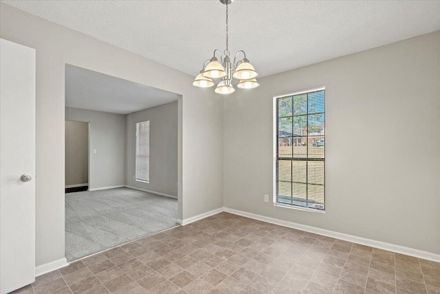 carpeted empty room with a textured ceiling and a chandelier