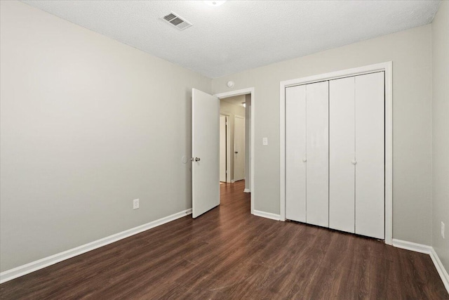 unfurnished bedroom featuring baseboards, visible vents, dark wood-type flooring, a textured ceiling, and a closet