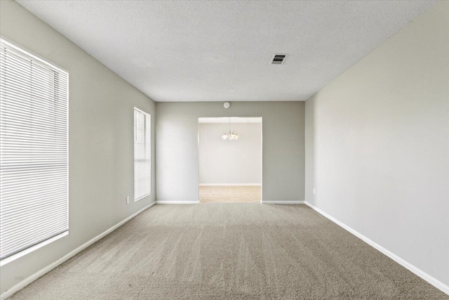 spare room featuring a chandelier, light colored carpet, and a textured ceiling