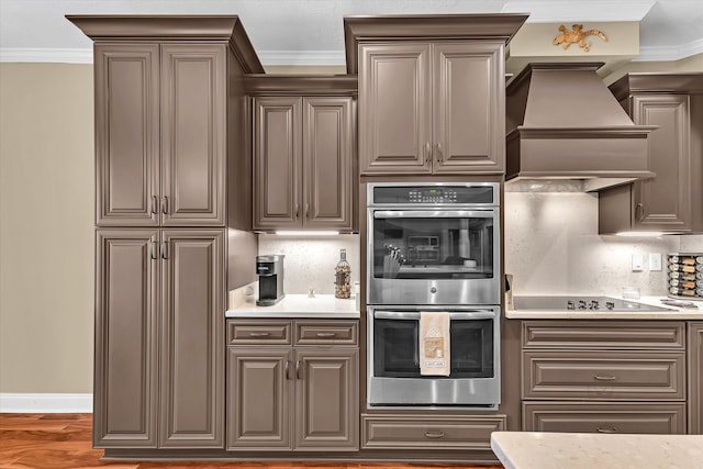 kitchen featuring custom exhaust hood, crown molding, dark hardwood / wood-style floors, stainless steel double oven, and backsplash