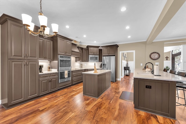 kitchen featuring a kitchen island with sink, hanging light fixtures, stainless steel appliances, dark hardwood / wood-style floors, and a kitchen bar