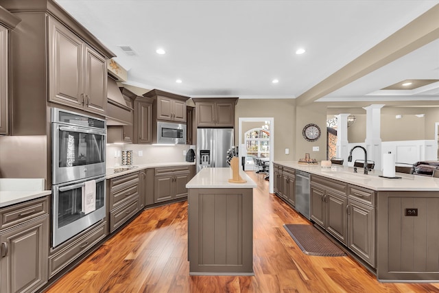 kitchen with sink, appliances with stainless steel finishes, ornate columns, a center island with sink, and light wood-type flooring