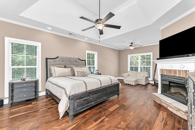 bedroom featuring ceiling fan, a tray ceiling, ornamental molding, dark hardwood / wood-style flooring, and a brick fireplace