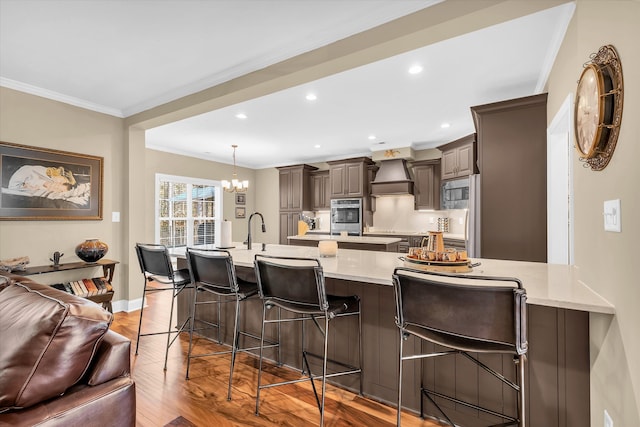 kitchen with a kitchen bar, custom exhaust hood, ornamental molding, kitchen peninsula, and light wood-type flooring