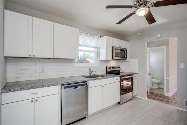 kitchen featuring appliances with stainless steel finishes, white cabinetry, light stone counters, and sink