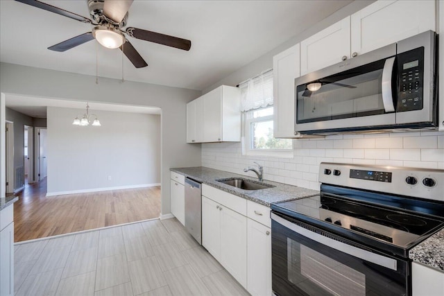 kitchen with stainless steel appliances, sink, white cabinetry, light stone counters, and tasteful backsplash