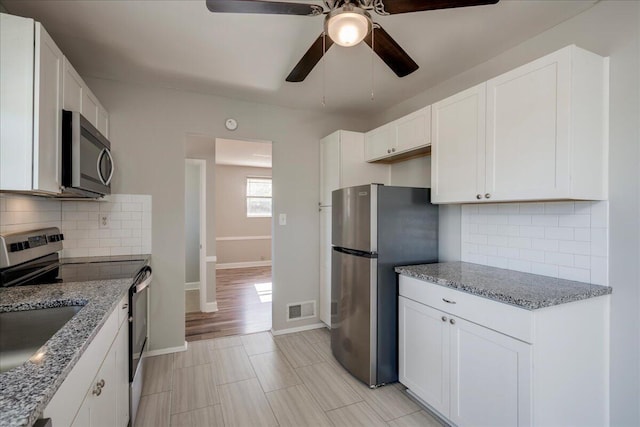 kitchen with light stone countertops, stainless steel appliances, white cabinetry, and decorative backsplash