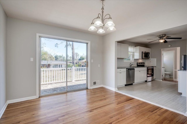 kitchen with white cabinetry, stainless steel appliances, hanging light fixtures, light hardwood / wood-style flooring, and tasteful backsplash