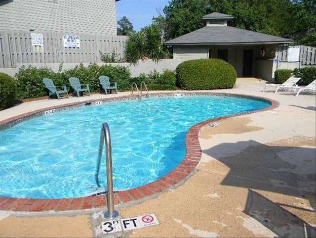 community pool with a patio area, an outbuilding, and fence